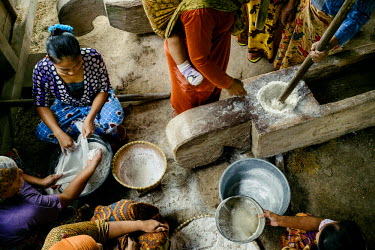 Women dehusking rice by hand. This activity is usually done in groups with long wooden sticks that act as pestles. The same sticks are also used to create percussive music that help time their poundin...