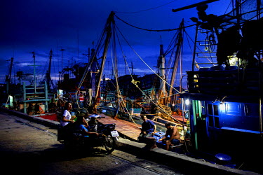 Fisherman on a Thai flagged fishing boat chat with women on shore at the docks in Songkhla.