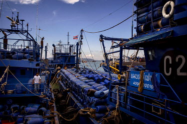 A man stands on a resupply boat that takes barrels of ice and other supplies out to fishing boats in the Thai fishing fleet in international waters and offloads their catch.