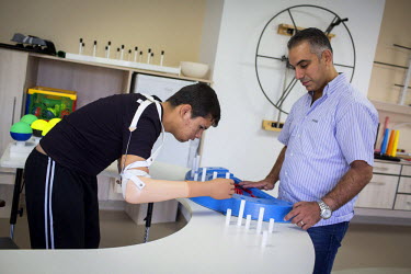 Nawaf, 15, learns to use his prosthetic arm during his rehabilitation with the assistance of Dr Ahmad Hammoud, from UNHCR partner the World Rehabilitation Fund, in Al Rahma Hospital, Tripoli. In mid-2...