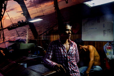 A fishing boat is reflected in the window of the bridge as two Thai fisherman rest on their resupply boat.