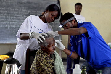 A health worker, specialised in hearing problems, checks the ear of an elderly woman during a camp clinic day.
