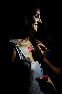 A girl get a pink neon heart painted on her chest, one of the many services supplied to the party goers by local people. The inhabitants on the small island have come to depend on the income brought i...