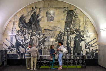 Passengers stand infront of a mural depicting Soviet heros at Novokuznetskaya Metro Station. Opened in 1943 its murals feature battles, military figures and the workers of the Great Patriotic War (Wor...