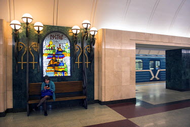 A woman sits on a bench beneath a stained glass depiction of Rostov churches at Novokuznetskaya Metro Station. Opened in 1943 its murals feature battles, military figures and the workers of the Great...