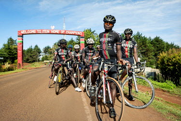 The Kenyan Riders, a Kenyan cycling team, gather before an arch over the road at the entrance of Iten with a slogan welcoming visitors to the 'home of champions'. The team train along the road between...
