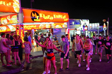 A group of youths walk up the street, passing a row of cheap take-away outlets. Thousands of young tourists visit Magaluf each year seeking cheap alcohol and fun. The new mayor Alfonso Rodriguez, has...