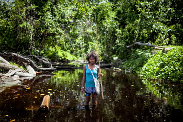 Christophilda Milik, 19, holding a fishing pole while she stands in a mangrove swamp near to where a logging company loads timber onto transport barges. Milik says: 'I used to catch fish in this swamp...