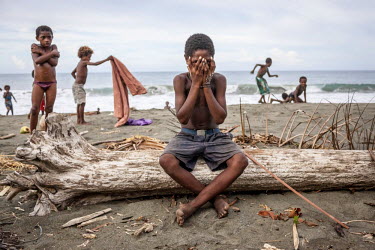 Nobert Mor, 13, sits on a dead tree trunk surrounded by children playing on the sea shore.