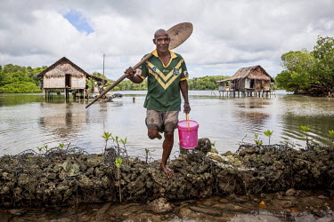 Mark Pokakes, 41, stands near his house in Bunai village on Pamachau Island. The only fresh water source on the island comes from rain. Pokakes is dressed in a shirt of the Australian rugy league team...