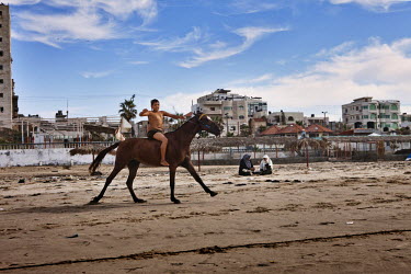 A boy on horse rides past two women on a beach in Gaza.