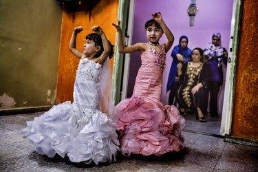 Two young girls in oppulent dresses dance for their uncle before a wedding celebration while women wait in the background.