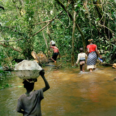 Children help an elderly woman with her belongings to cross a river.