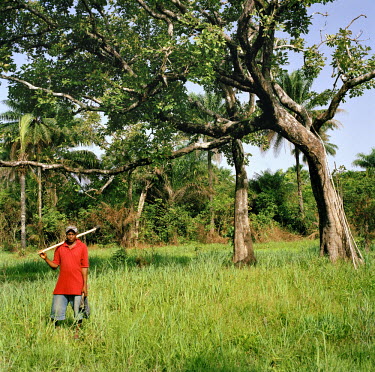 Momodu Kanu stands in a field with farm tools.