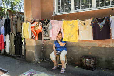 A woman sits beneath a line of clothes she is selling at a flea market.