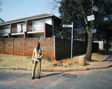 A man in a creme coloured suit stands on a street corner in the black middle class suburb of Cresta.