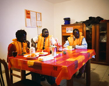 Three Senegalese migrants have afternoon tea and watch football on TV after working outside.