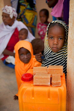 A young girl stands beside a water container with soap, distributed by Oxfam to help with sanitation and hygiene at the Azel Treatment Centre, a small community health centre, largely dealing with mal...