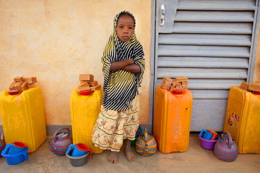 A young girl stands beside water containers with soap, distributed by Oxfam to help with sanitation and hygiene at the Azel Treatment Centre, a small community health centre, largely dealing with maln...
