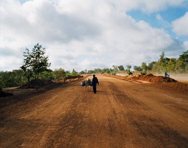 A man and a donkey walking on the foundations of a highway in the east of the country near Kitui.