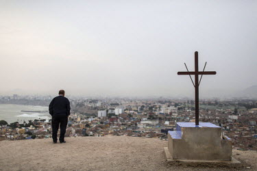 A man stands beside the cross on Morro Solar looking down over the district of Chorrillos.