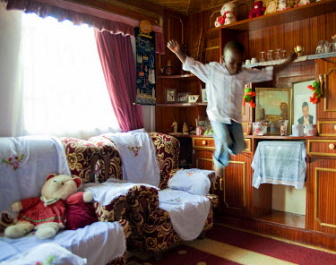 A boy practices long jump from an arm chair in his aunt's middle class home while waiting to go to church.