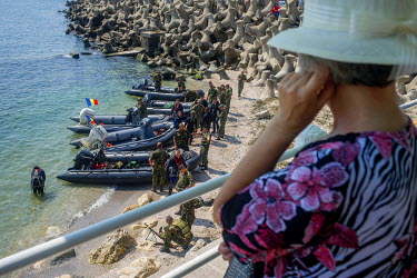 Navy recruits checking and unloading their equipment after they performed a parade on the sea during Romanian Navy Day. Watching from the seaside promenade is the mother of one of the officers and she...