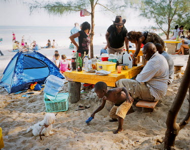 A boy plays with the family dog as they enjoy Sunday lunch on the beach near Maputo.