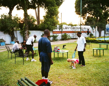 A member of staff watches over the child of an expat at the Douala tennis club while club members socialise between activities.