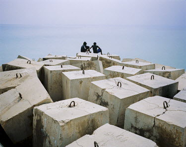 Two young men relax on concrete blocks at the seawall in Luanda, the capital.