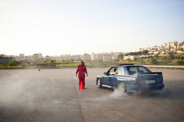 A motor mechanic test drives a car around Betty on a training track in Ramallah. Betty is one of five women who make up the "Speed Sisters", an all women car racing team, the only one of its kind in t...