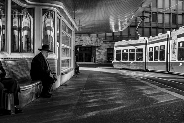 An orthodox Jewish man sits at a tram stop in Paradeplatz.