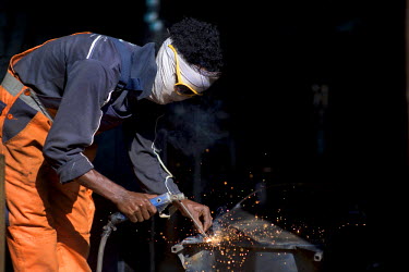 A man welding metal with a self-made protective mask at the Medeber metalwork market. This huge market is the centre of Asmara's recycling industry.