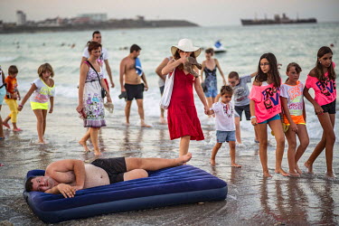 A man lies on an inflatable mattress as people leave the beach at the end of the day. In the background the wreck of a Greek ship stranded on the shore in 1968 can be seen. It has now become the symbo...