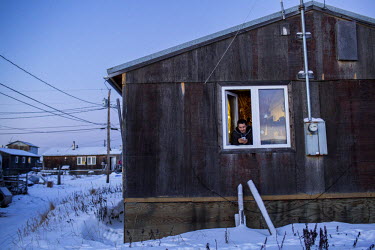 A man leans out of a window checking his mobile phone. Shishmaref is a barrier island with a population of less than 600 Alaska native Inupiaq people located 30 miles south of the Arctic Circle. The i...