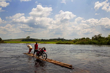 A bank employee and his motorbike are ferried across a river on a flimsy bamboo raft. A team from the bank took to the road for several weeks to travel the remote region in order to pay state employee...