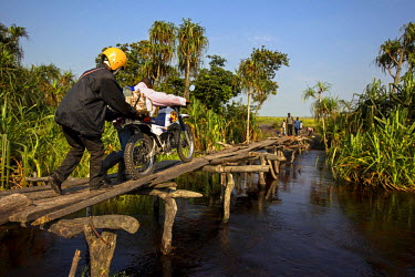 Trust Bank staff members wheel their motorbike over a narrow flimsy river bridge. A team from the bank took to the road for several weeks to travel the remote region in order to pay state employees an...