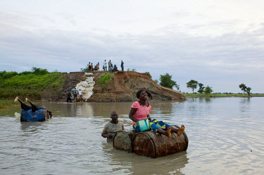 A woman laughs as she if ferried on oil barrels across a flooded river that has destroyed the bridge and stranded the population for many days.