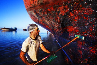 A worker scrubs down the hull of a traditional Iranian Lenj boat being repaired in the Gouran boatyard. Holes in the hull are filled with cooton wadding and the ship given a coat of paint. Gouran is t...