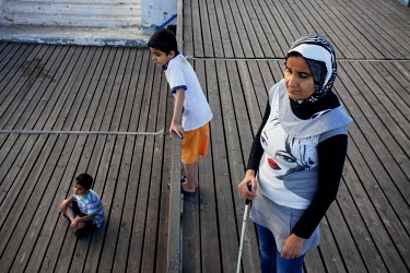 Thirty four year old Jihan with her sons Ahmed and Mohammad, aged five and seven, on a jetty near their home in the Lavrio refugee camp.  They left Damascus with Jihan's husband Ashraf, to escape the...