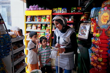 Thirty four year old Jihan shopping in a small grocery store with her sons Ahmed and Mohammad aged five and seven. They are living close by in the Lavrio refugee camp.  They left Damascus with Jihan's...