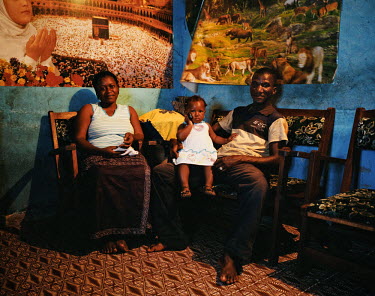 Fofana Adama, a middle class man, poses in his living room with his wife and his daughter.