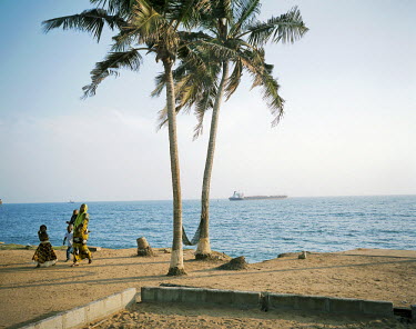 A family goes for a walk along the seashore in Abidjan with a freight ship visible in the distance.