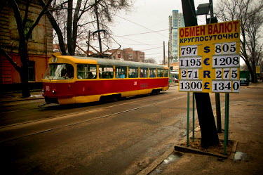 People sitting on a tram as it passes a currency exchange board on a during a cold winter day.