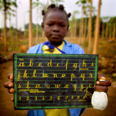 A girl on her way to school holding a black board with the alphabet wriiten on it.