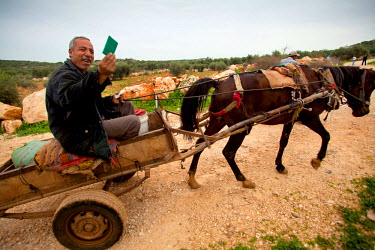 A farmer riding a horse drawn cart holds up his security pass that enables him to pass through Israeli checkpoints.