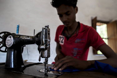 Nazeeb sews at a machine at his home. He was trafficked and worked in a factory where he had to produce 3,000 zips an hour. He escaped and is now running a poultry farm from his home.