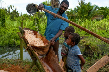 Children watch on as a man filters crushed sago palm during the production of sago starch, a staple food in PNG and beyond.