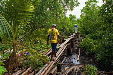 A man crosses a rickety bamboo footbridge to a toilet on the other side.