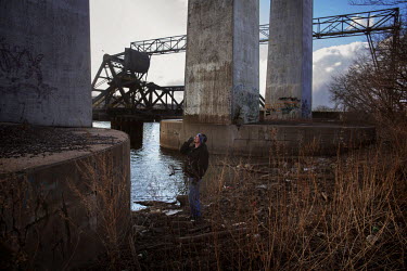 John Bryant (35) smokes while standing beside the Rouge River in Delray. The area is cluttered with chemical factories and oil refineries. Bryant says: 'This area looks like a dump. People are dumping...